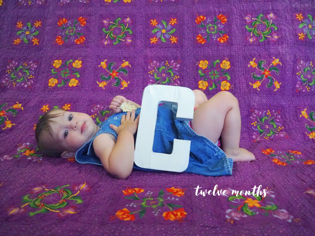 baby girl lying on a quilt with the letter "C", and "twelve months" written below